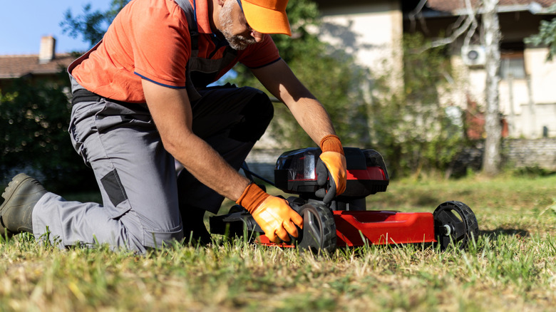 Man performing maintenance on the deck of a red lawn mower