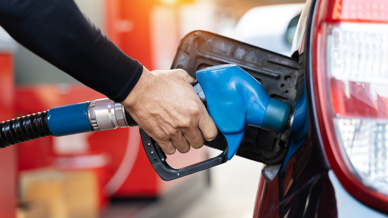 Hand holding blue gas pump in car gas tank