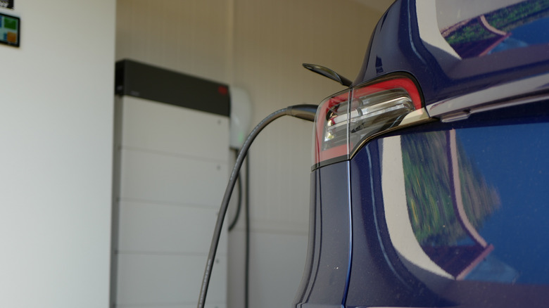 A close-up of a blue Tesla rear-end while being charged on a home garage charger.
