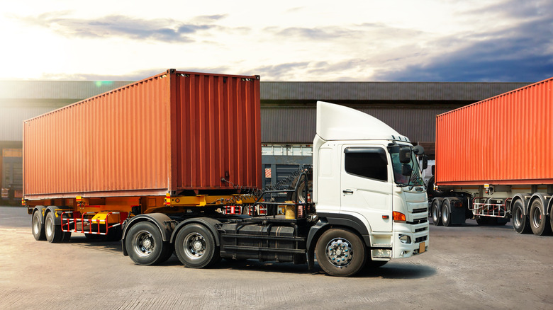 Semi truck's carrying containers backing into a delivery terminal.
