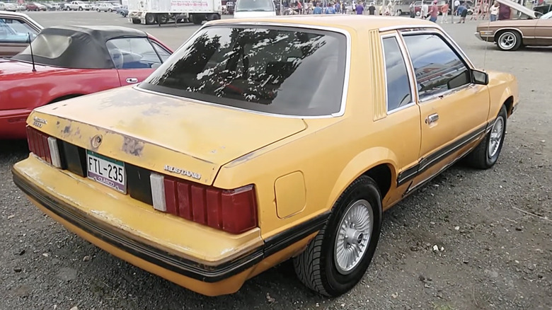 Rear of a 1980 Ford Mustang in yellow parked on gravel