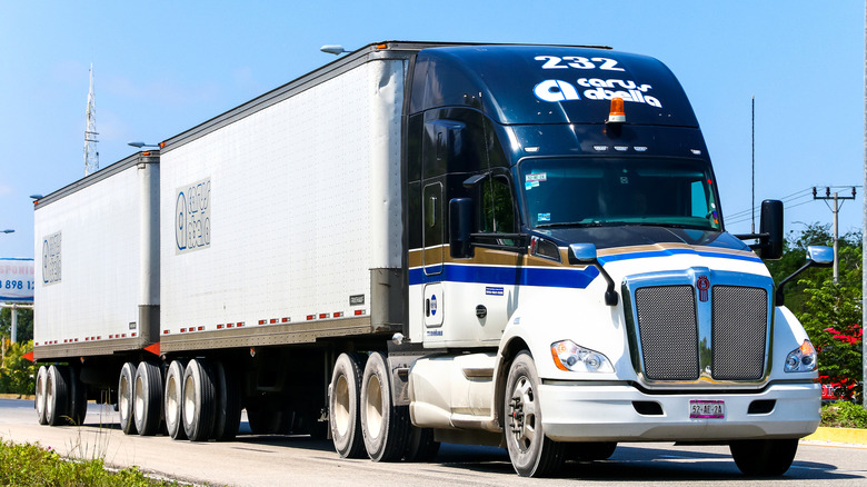 A front 3/4 shot of a blue and white double bed Kenworth T680 semi-truck cruising down the road.