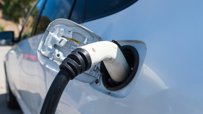 A white electric or plug-in hybrid vehicle plugged in to charge