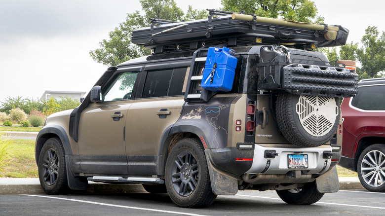 A heavily-modified overlanding Land Rover Defender parked with a roof-mounted tent.