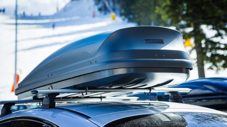 A close-up of an unbranded silver roof box, snowy ski course in the background