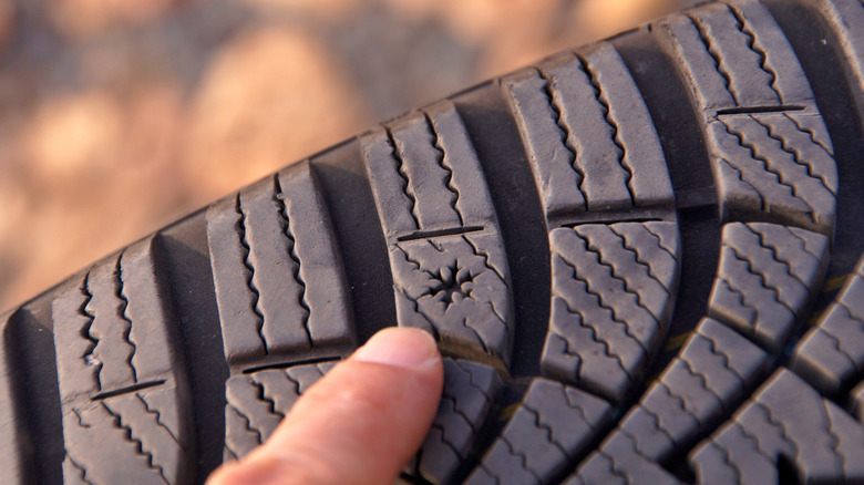 Finger pointing at a tread wear indicator on a used car tire