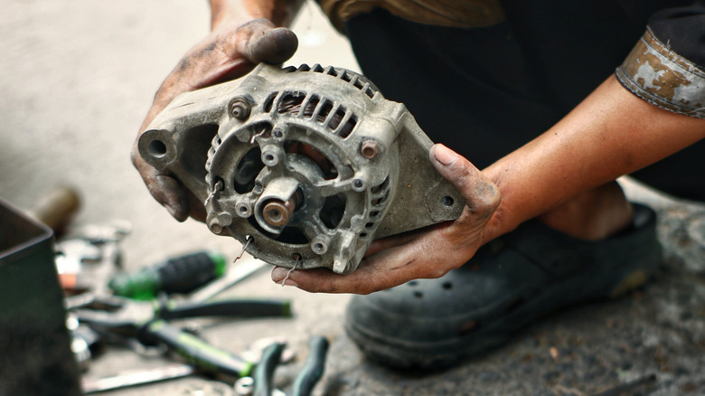 A mechanic with dirty hands holding a worn-out alternator