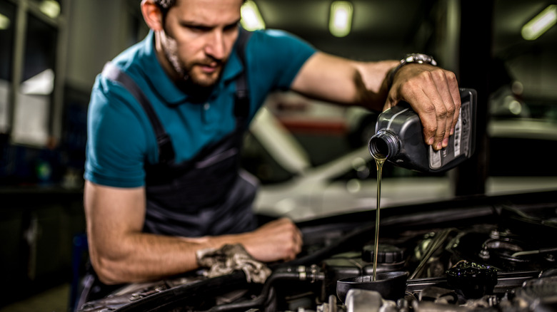 Auto mechanic changing oil on car engine.