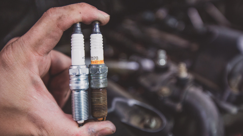 Hand holding a new spark plug next to an old spark plug
