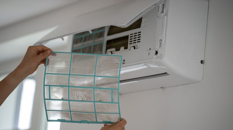 Hands holding a clean filter in front of a mini-split AC air handler.