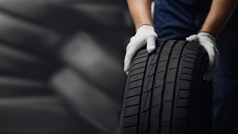 mechanic holding new tyre on background store