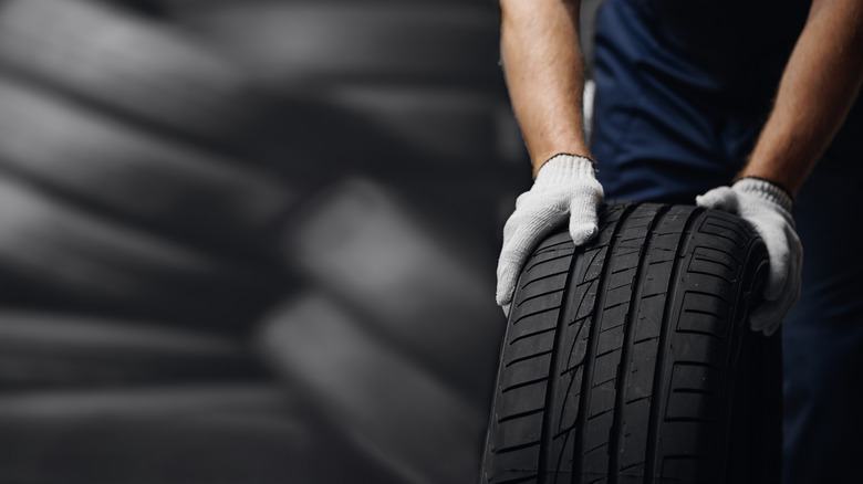 mechanic holding new tyre on background store