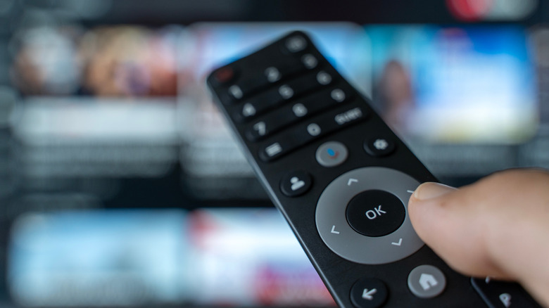 A close-up of an unidentified remote control, out-of-focus TV in the background displaying what appears to be YouTube