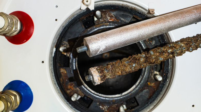 new and corroded anode rods side by side above water heater tank opening