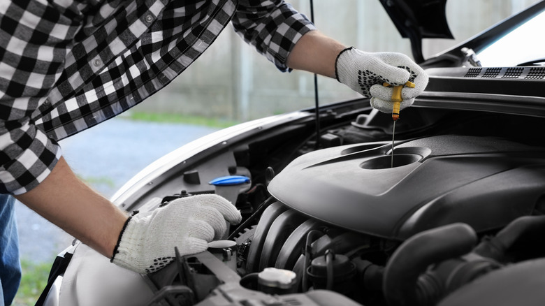 Mechanic hands checking motor oil level with dipstick in car.