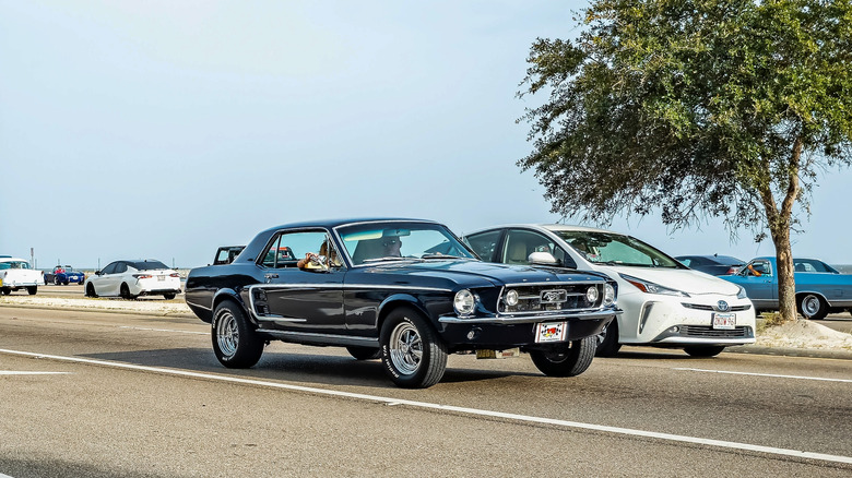 black 1967 Ford Mustang GT hardtop coupe driving in traffic on coastal highway