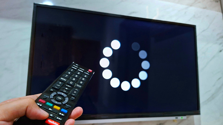 A man pointing a remote at a smart tv, with a loading screen being shown on the tv screen