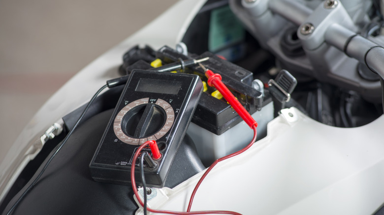 A person testing their motorcycle battery's voltage.