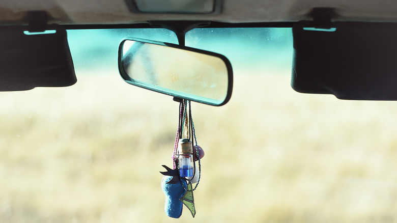 Various accessories hanging from the rear view mirror of a vehicle.