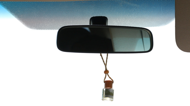 An air freshener bottle hanging from a car's rear view mirror.