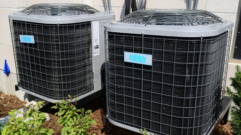 Two air conditioners next to each other by a house.