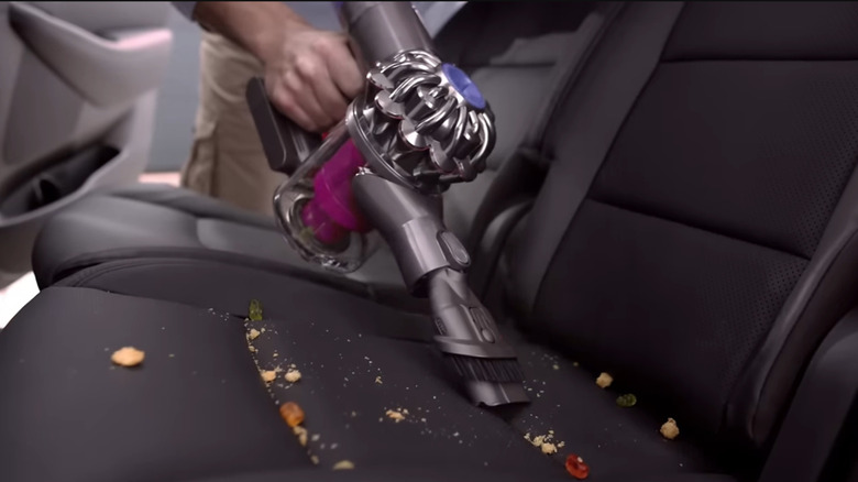 A person using a Dyson V6 vacuum to clean a car seat