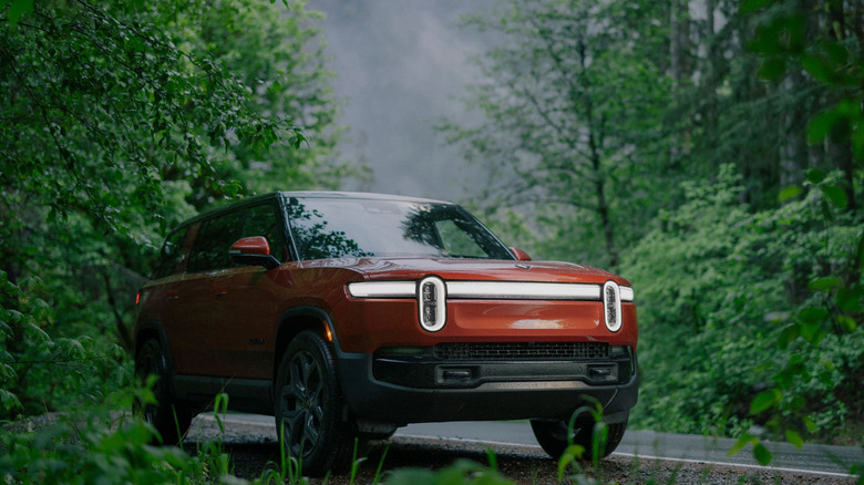 A Rivian R1S in orange parked beside a forest road, front 3/4 view