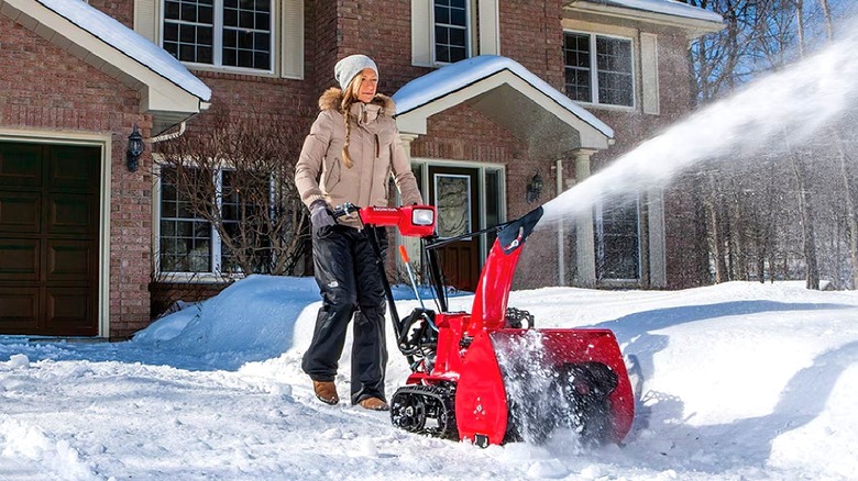 Blonde woman in coat blowing driveway of snow with red Honda snowblower
