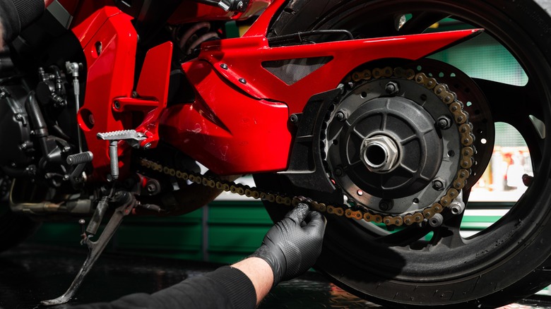 Motorcycle mechanic checking a chain for proper tension