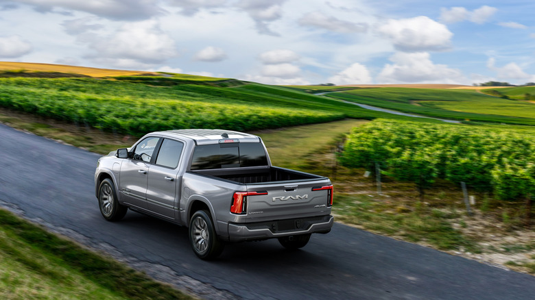 2026 RAM driving on farmland road, rear-left 3/4 view