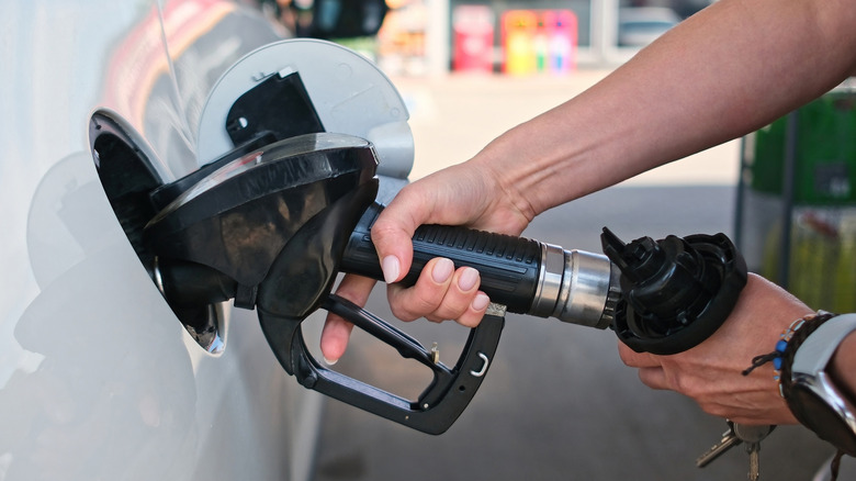 Close-up of hands holding a black gas nozzle while filling a car up.
