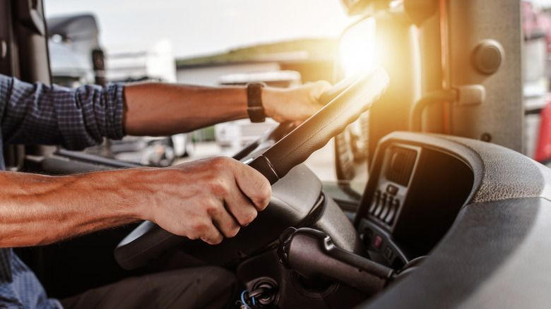 A close-up view of a truck driver's hands gripping the steering wheel inside a semi-truck cab.