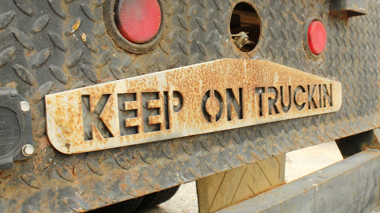 A close-up of the rear of a rusty flatbed truck with a metal plate that reads "KEEP ON TRUCKIN."