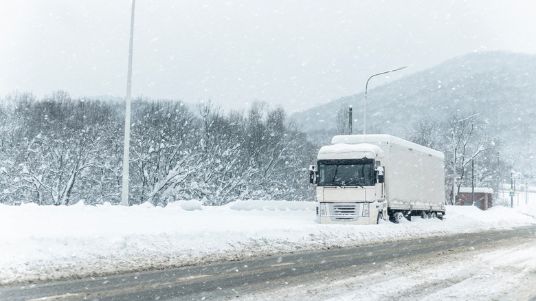 A white semi-truck stuck on a snow-covered road during heavy snowfall.