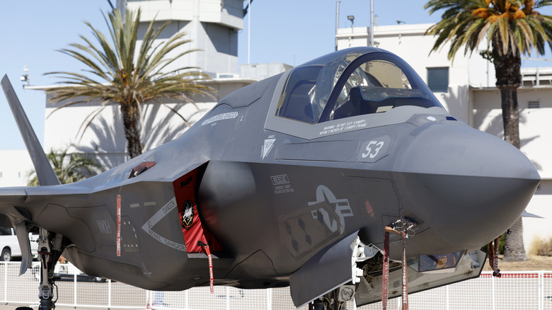 Ab F-35 Lightning II parked at an air base with palm trees and the control tower in the background,