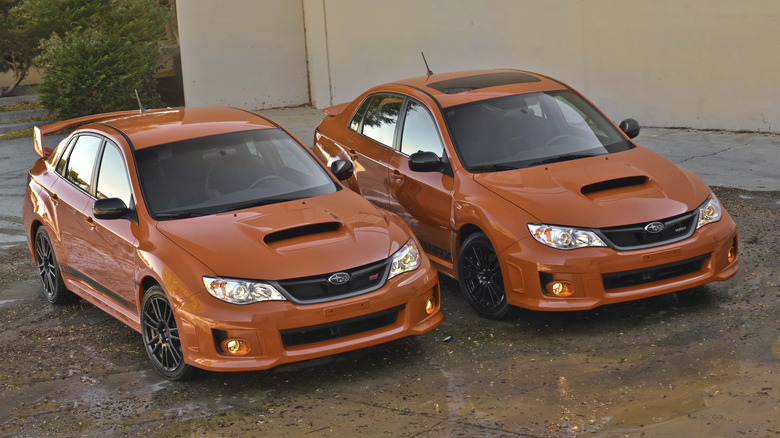 An orange Subaru Impreza WRX and an orange WRX STI models side by side, front view