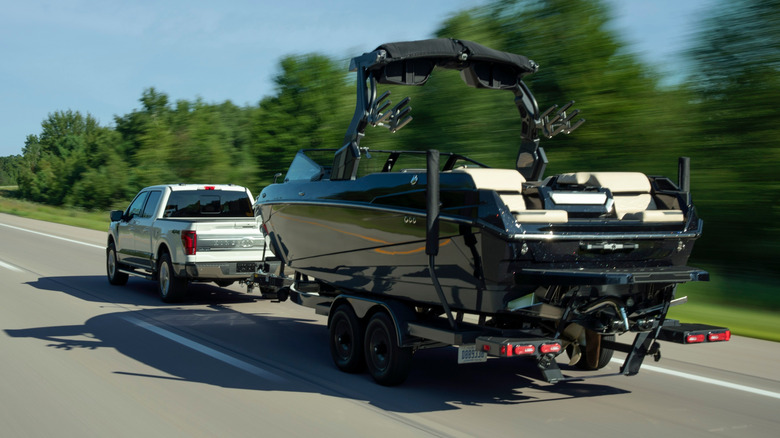 Rear view of white Ford F-150 towing large black boat on highway.