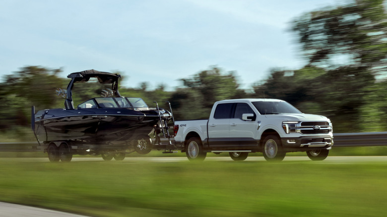 White Ford F-150 towing boat on highway.