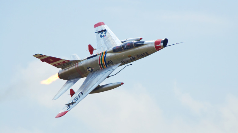 A F-100F Super Sabre flying at an angle, red painted tips