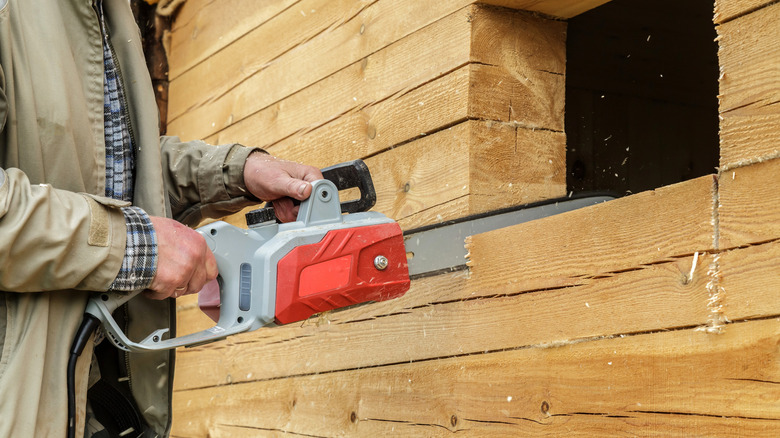 A person using a gray and red chainsaw to cut some wood