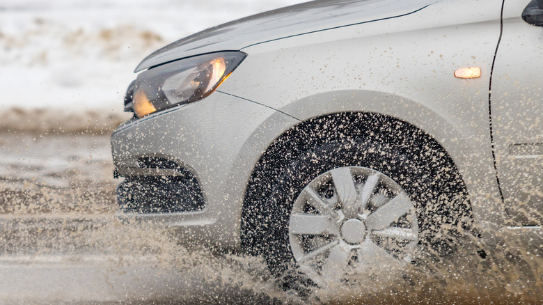 A car driving fast through a muddy puddle, close-up photo showing the fender and the wheel
