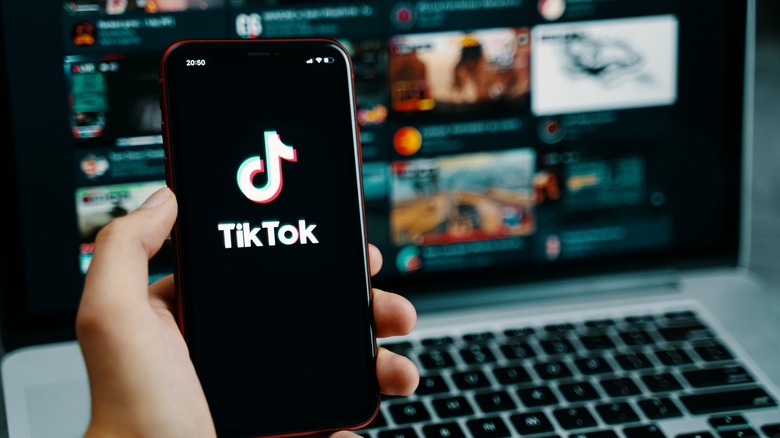TikTok open on a phone with a laptop in the background
