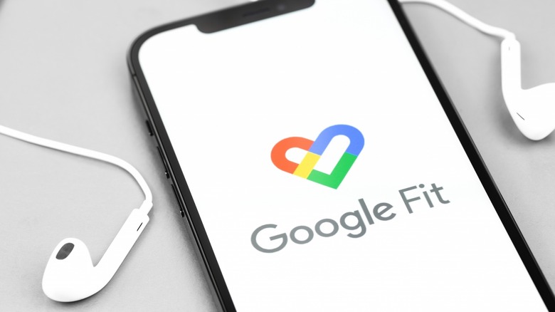 Google Fit on a mobile phone with earbuds sitting next to them
