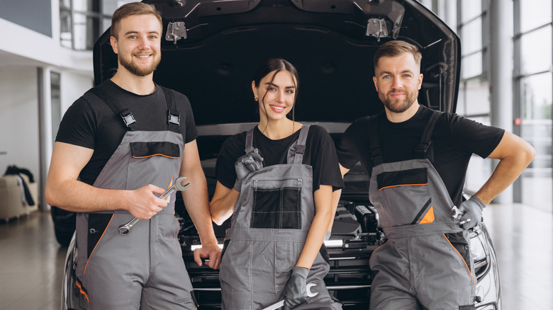 Three mechanics standing in front of a car with the hood open