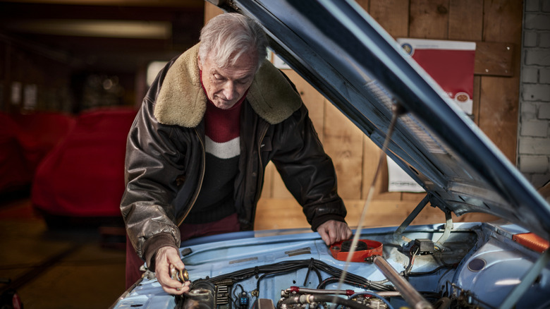 Elderly man checking the coolant on a classic car