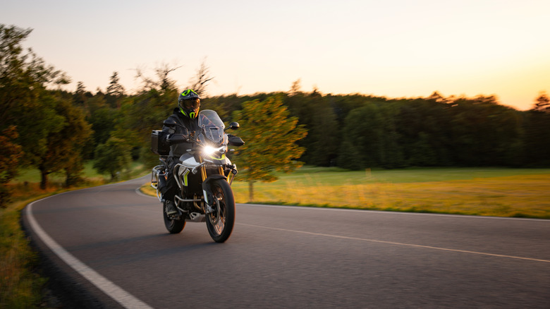 Person riding motorcycle on empty country road at dusk