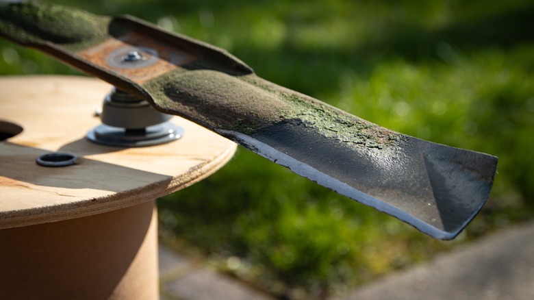 A lawn mower blade with caked on dirt and grass needs to be cleaned before balancing.