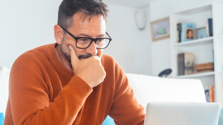 A man wearing glasses focuses on a laptop