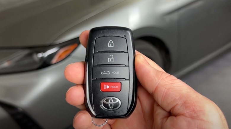 A hand holding a key fob in front of a 2025 Toyota Camry.