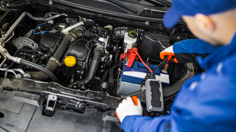 An auto mechanic uses a portable jump starter on a car battery